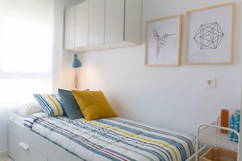Habitación renovada de la residencia con cama a rayas y flexo azul